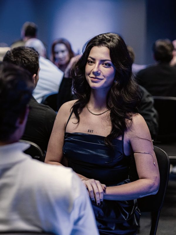 Kath Zaparoli sorrindo, sentada no meio da plateia de um evento