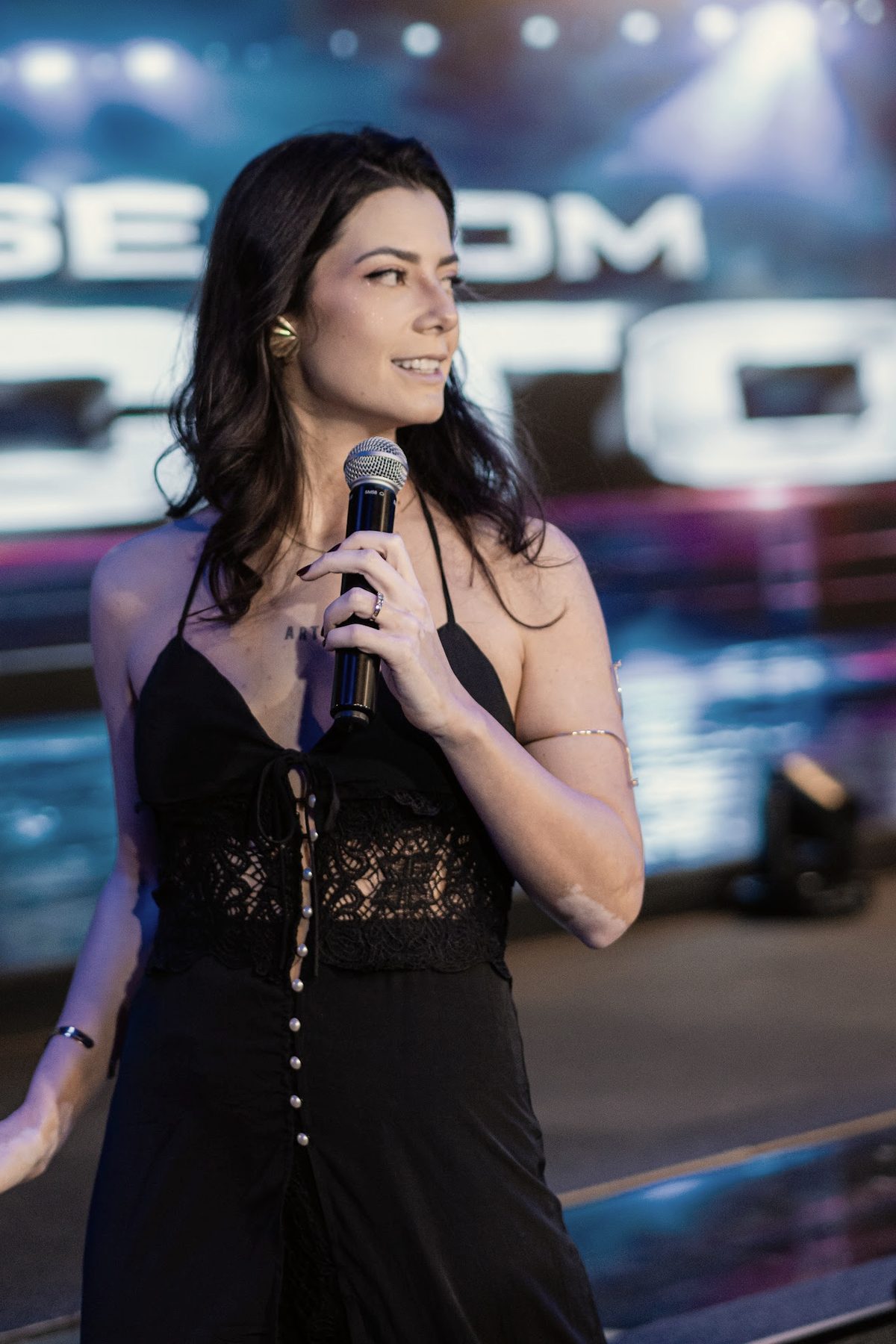 Kath Zaparoli sorrindo no palco do Comunique-se com Impacto, em São Paulo, com o microfone na mão